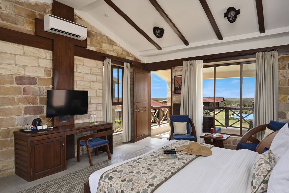Habitación de hotel con una cama grande, un escritorio con televisor y vista a una piscina y al paisaje.