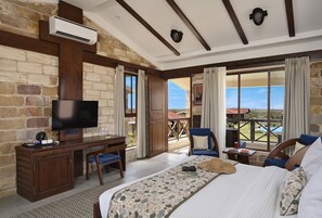 A hotel room with a large bed, a desk with a television, and a view of a pool and landscape. - The Blackbuck Trails Velavadar (Bhavnagar)