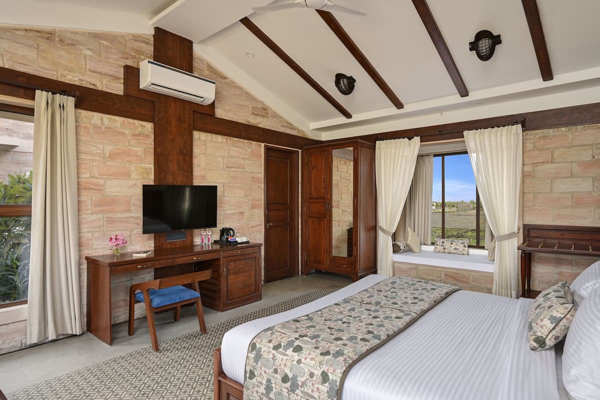 Un dormitorio con cama, televisión, escritorio y ventana con cortinas.