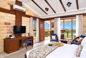 A hotel room with a large bed, a desk with a television, a chair, and a view of the outdoors. - The Blackbuck Trails Velavadar (Bhavnagar)