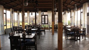 Un vaste espace dédié à la salle à manger, avec de nombreuses tables et chaises, de grandes fenêtres dotées de rideaux et des luminaires suspendus.