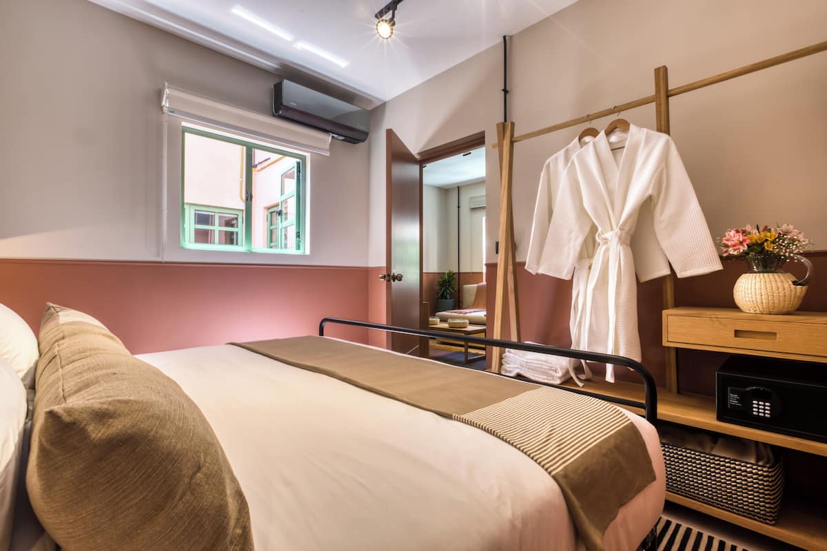 A hotel room with a bed, a bedside table with a lamp, a window, and a mirror.