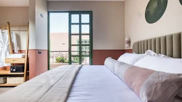 Habitación de hotel con una cama grande, una mesita de madera, una bata colgada y vistas al balcón exterior.