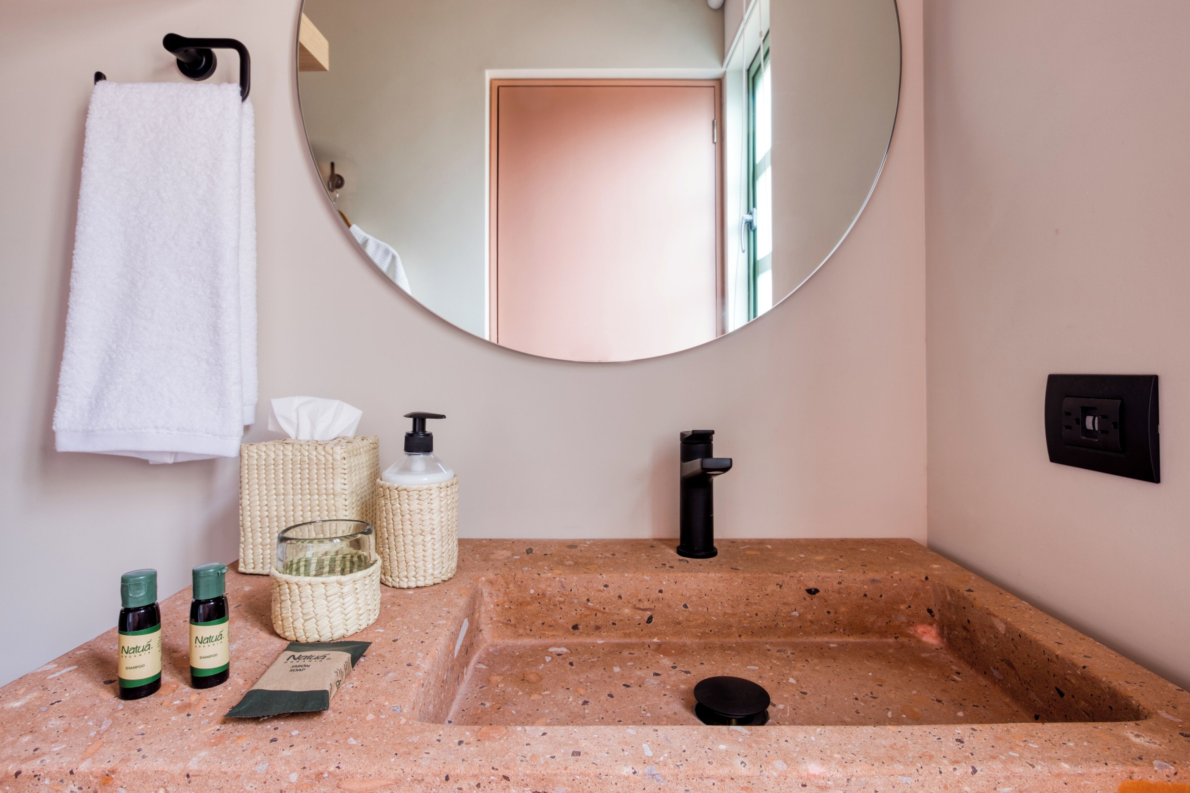 A bathroom with a granite sink, a round mirror, a towel rack, and toiletries.