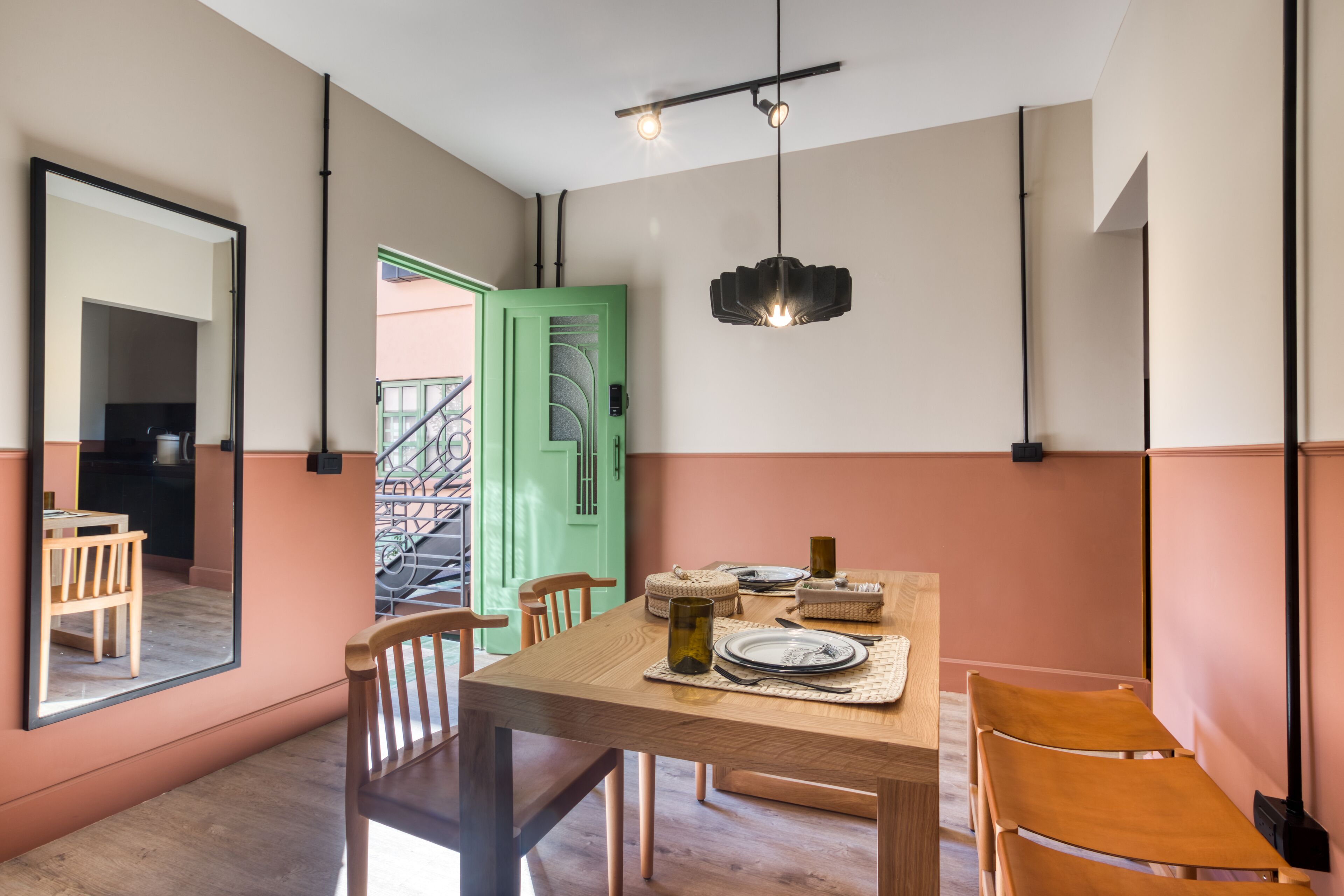 A dining area with a wooden table set for two, a green door, and a staircase leading to an outdoor area.