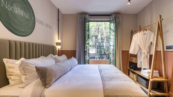 Habitació d'hotel amb un llit gran, un panell de fusta al capçal, un suport de tovalloles fixat a la paret i vista a arbres per la finestra.