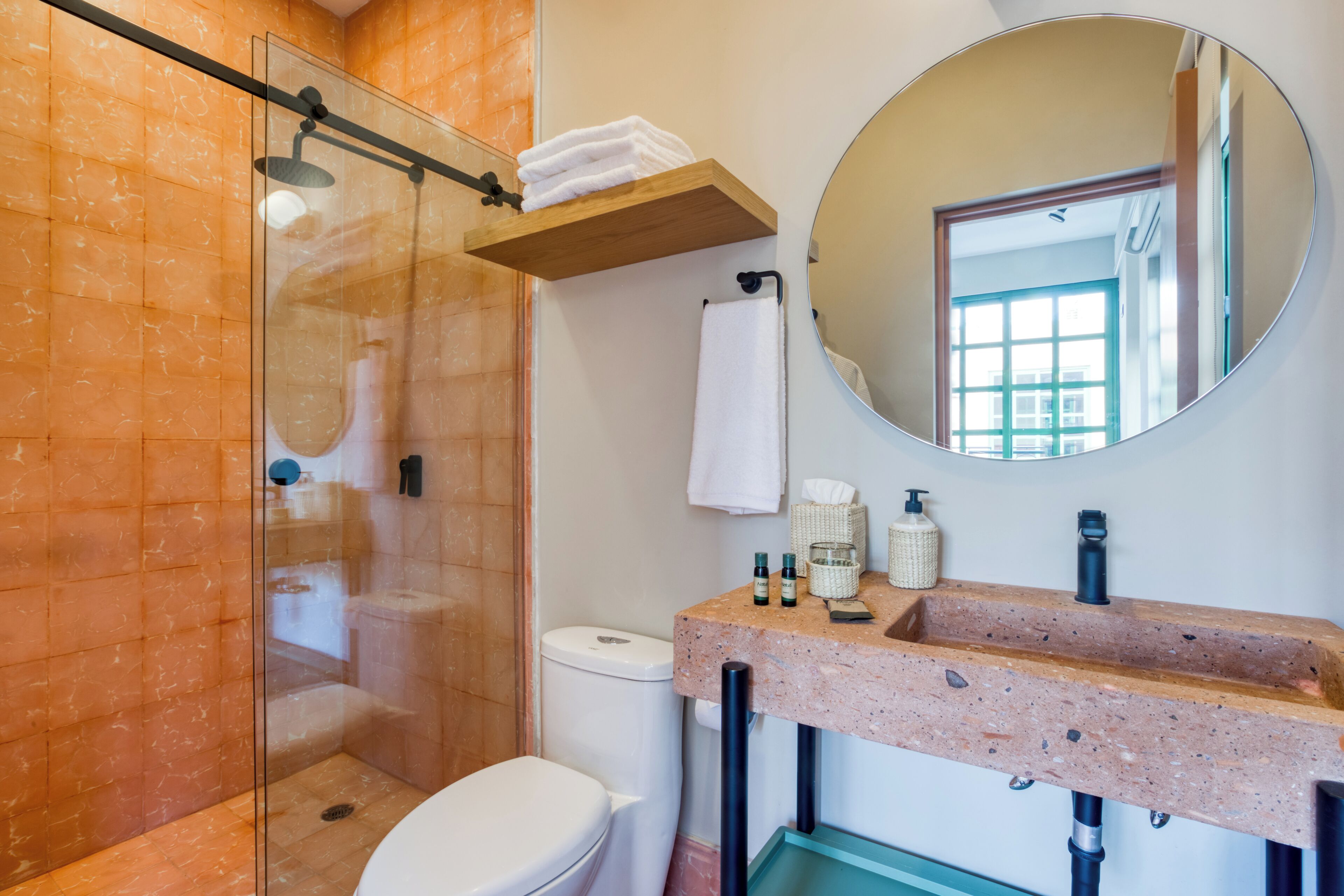 A modern bathroom with a glass-enclosed shower, a white toilet, a sink with a marble countertop, and a round mirror.