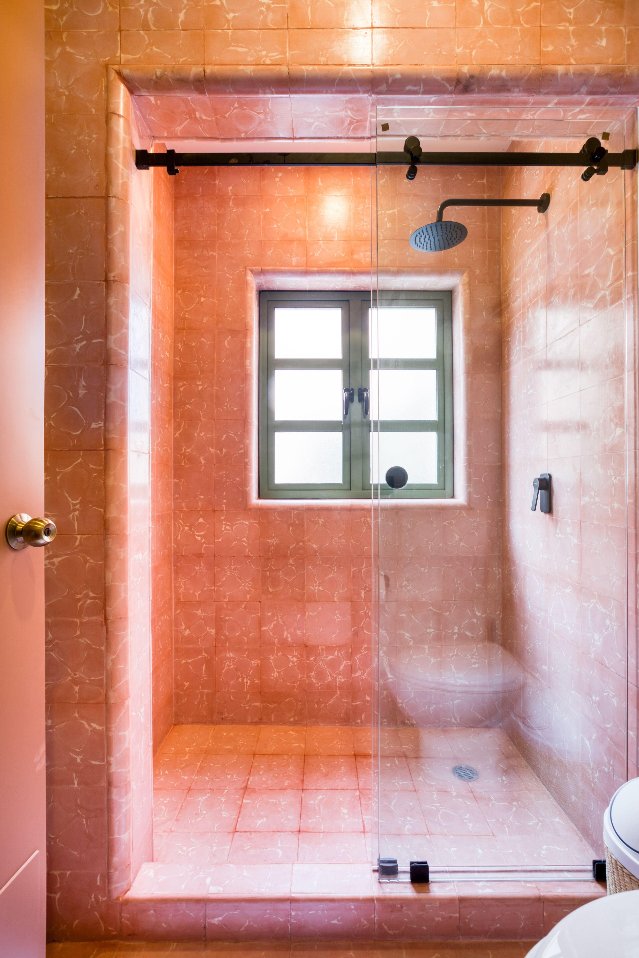 Chuveiro com porta de vidro, janela e vaso sanitário.