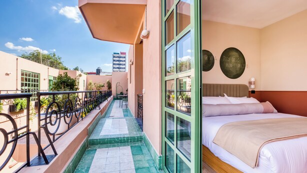 A hotel room with a balcony, a bed with white linens, and a view of the cityscape. - Casa Oliva (Mexico City)