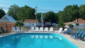 A swimming pool with white lounge chairs and a red car in the background. - The Palms Motel (Geneva)