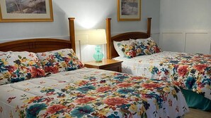 A hotel room with two beds, each with floral bedding, wooden headboards, and a nightstand with a lamp. - The Palms Motel (Geneva)