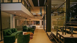 Un interior moderno con una zona de estar central que incluye sofás y sillones verdes, una mesa de centro de madera y una barandilla de vidrio con vistas a un nivel inferior.