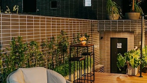 Un edificio moderno con un letrero que dice "urban", una terraza de madera, una silla de mimbre y plantas en macetas.