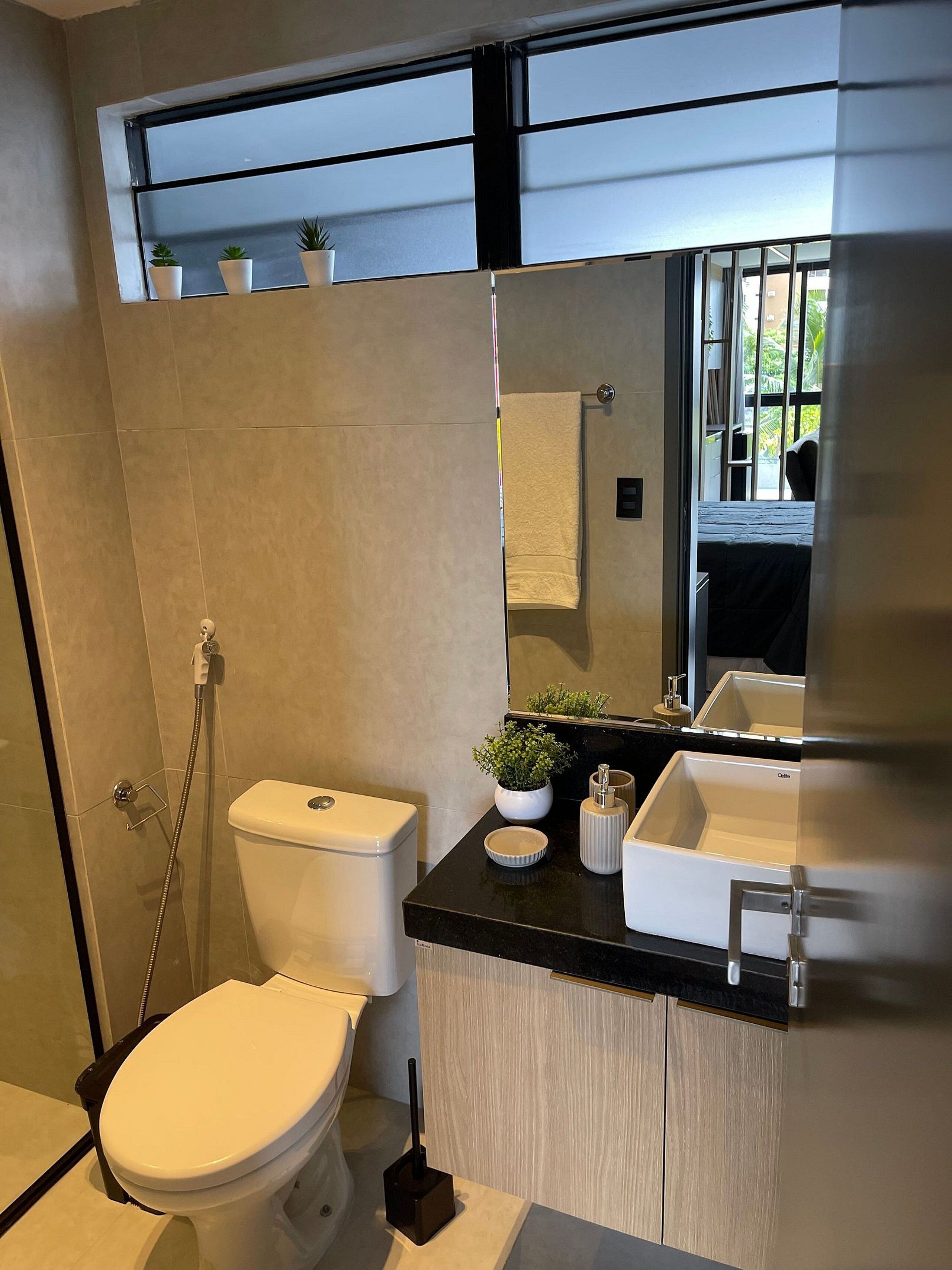 Un bagno moderno con toilette, bidet e lavandino. Sul davanzale ci sono piante in vaso e uno specchio sopra il lavandino.