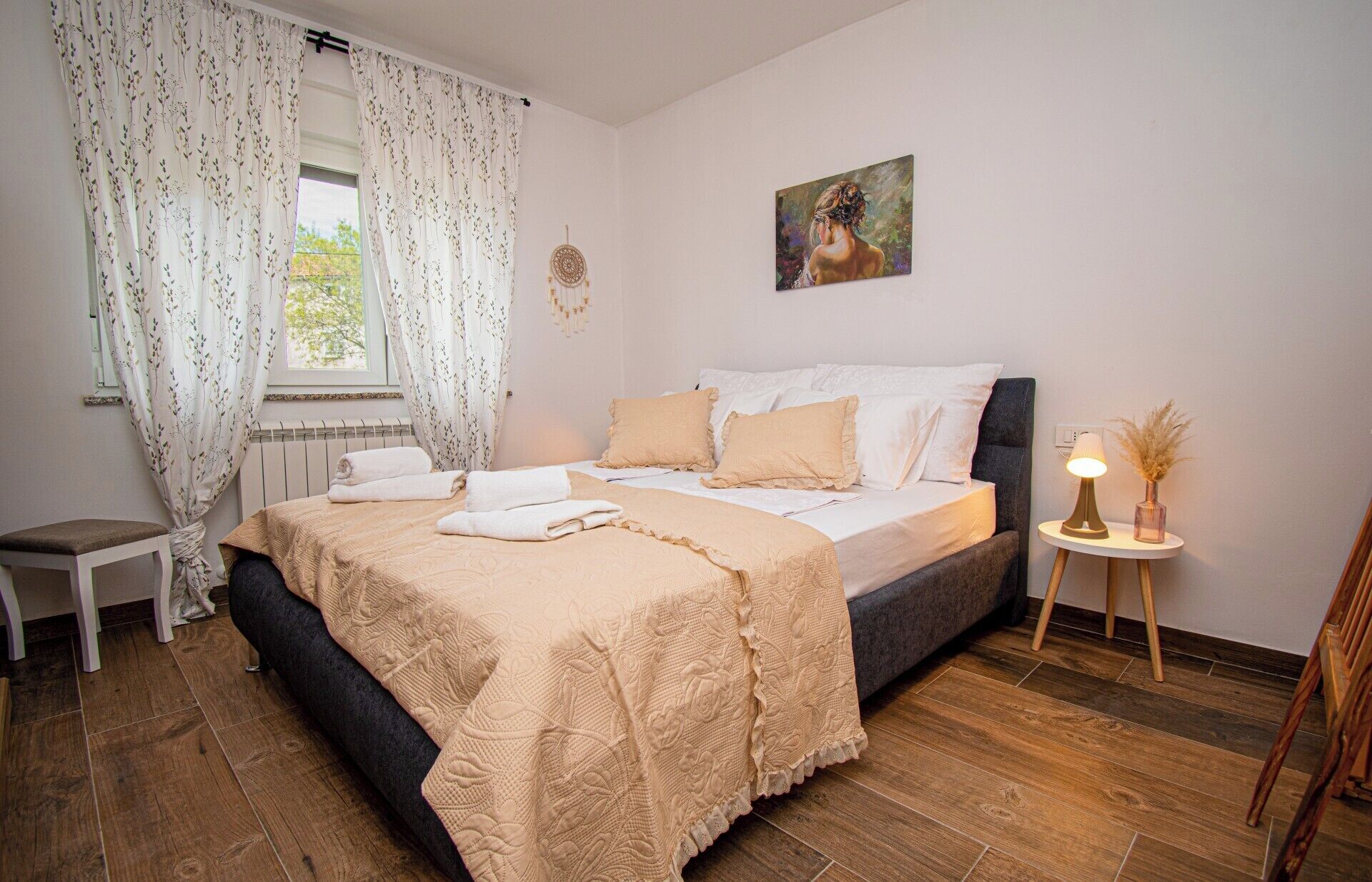 Un dormitorio con cama, una mesita de noche con lámpara, una silla y una ventana con cortinas.