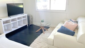 A modern living room with a white sofa, a glass coffee table, and a flat-screen TV on a white stand.