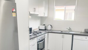 A modern kitchen with white cabinets, a stainless steel refrigerator, a toaster, a kettle, and a dishwasher.