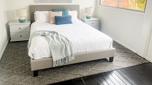 A bedroom with a bed, two nightstands, a window, and a painting on the wall.