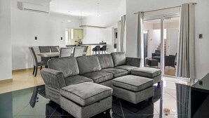A modern living room with a sectional sofa, a dining area with a table and chairs, and a staircase leading to another level.