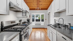 A modern kitchen with white cabinets, a stainless steel stove, and a wooden ceiling.