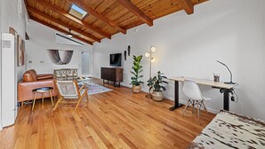 A spacious room with a wooden ceiling, a sofa, a dining table, a TV, and a desk with a chair.