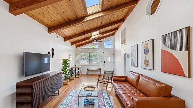 A spacious living room with a wooden ceiling, a leather sofa, a flat-screen TV, and artwork on the walls.