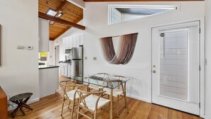 A modern kitchen with a glass dining table and chairs, wooden flooring, and a white door with blinds.