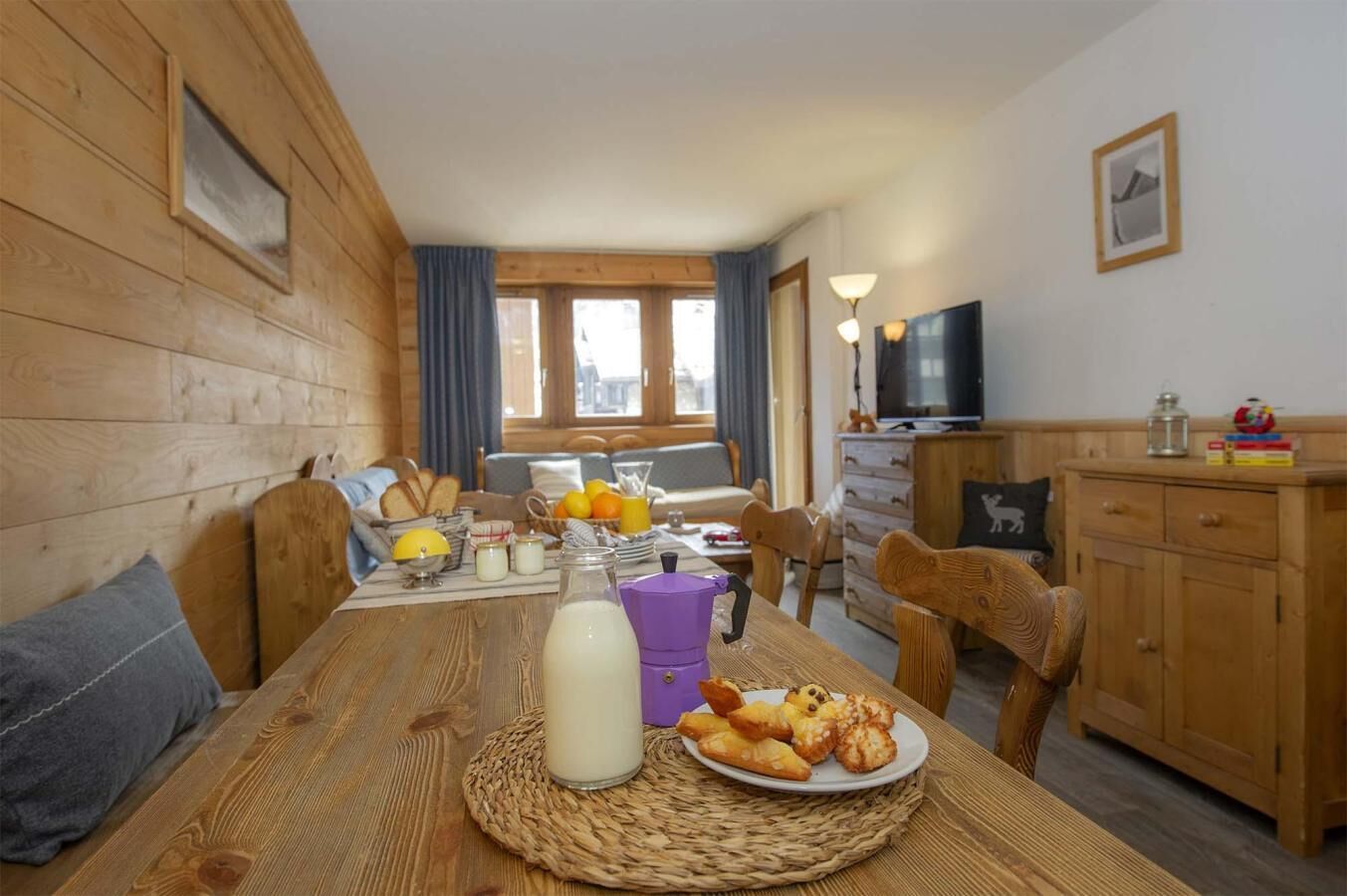 A cozy wooden cabin with a dining table set for breakfast, a television, and a kitchen area.