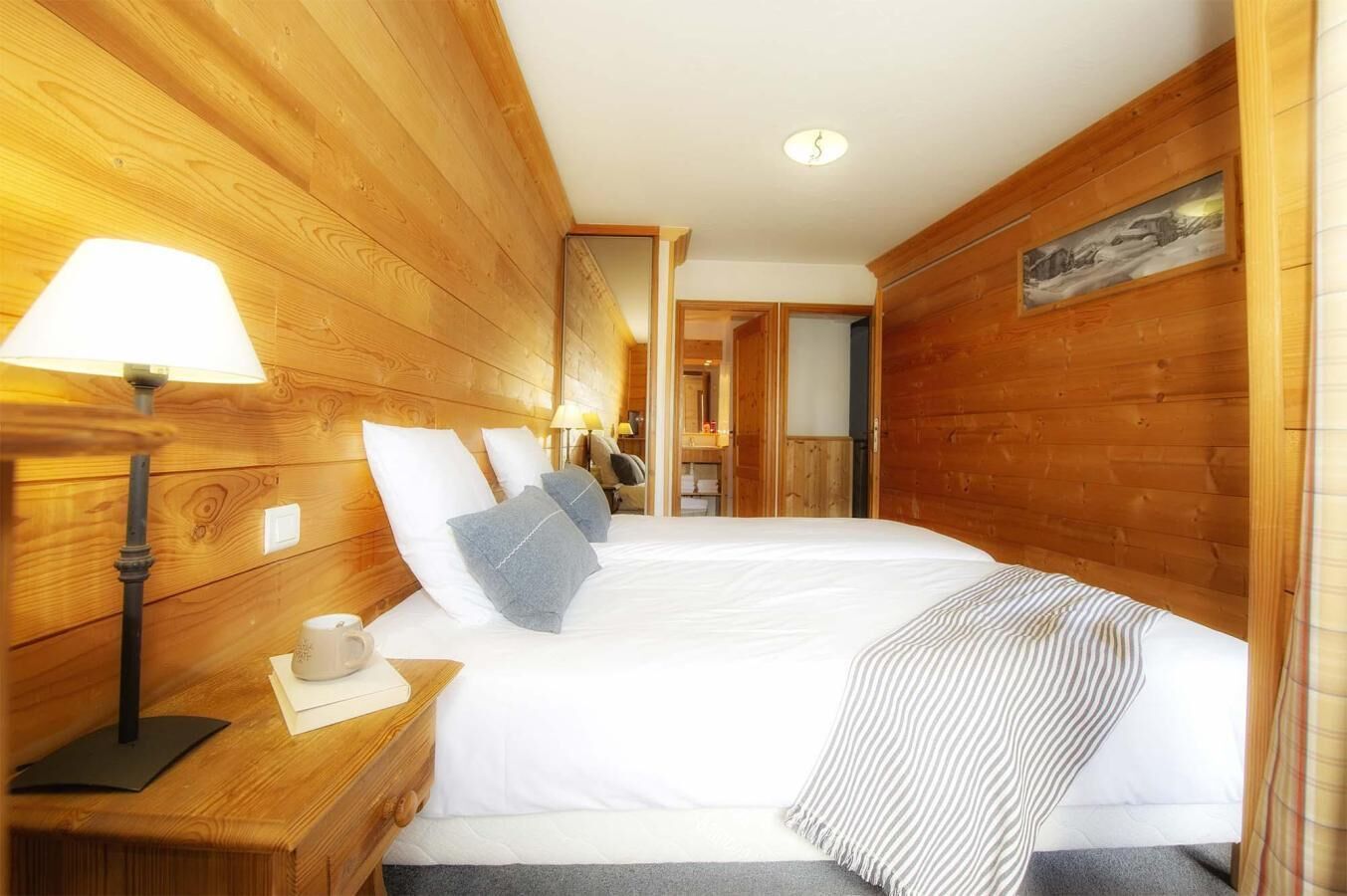A wooden room with a bed, a nightstand, a lamp, and a painting on the wall.