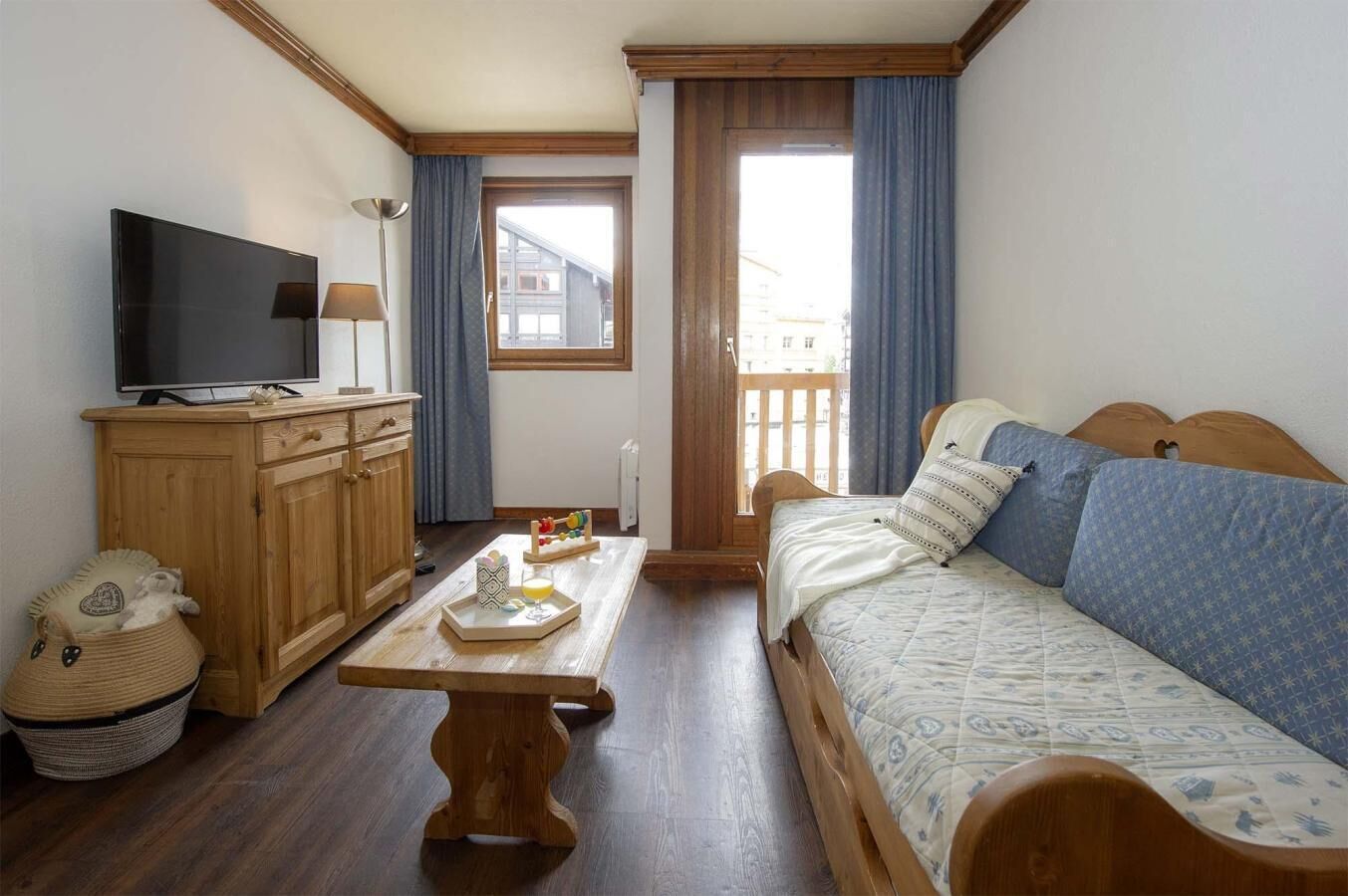 Une pièce confortable avec un lit en bois, une télévision, une armoire en bois et une fenêtre avec des rideaux.