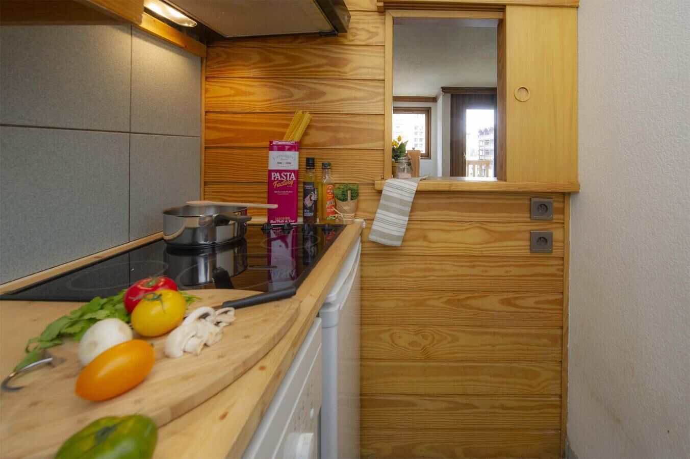 A compact kitchen with wooden cabinets, a stove, and various cooking utensils.