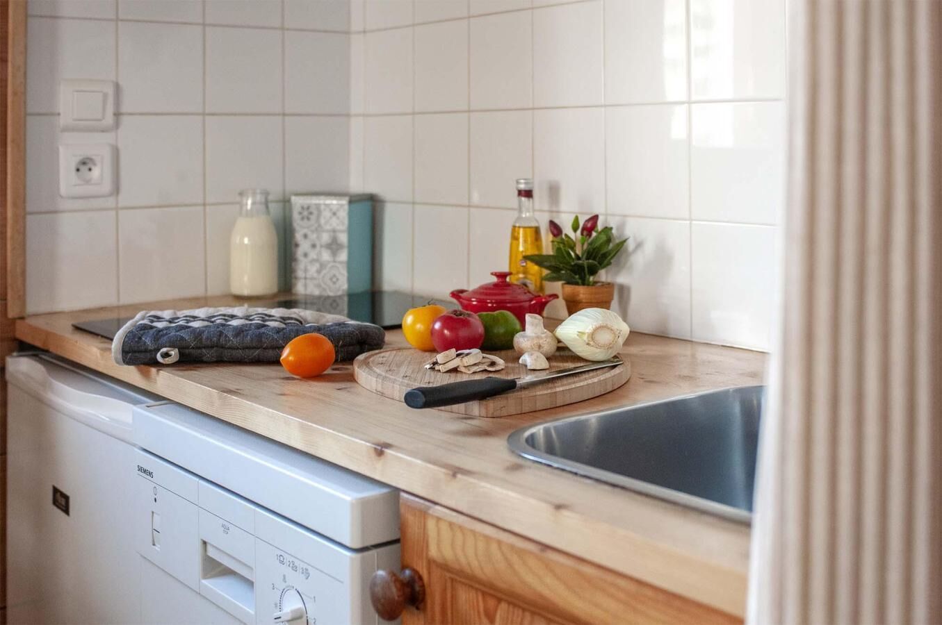A kitchen with a wooden countertop, a sink, a dish rack, and a Siemens dishwasher.