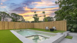A rectangular pool with a wooden fence and chairs, surrounded by green grass and trees. - Peaceful and Spacious Pool home in Jensen Beach! RV-Boat Prkg-Fenced Yrd (Jensen Beach)