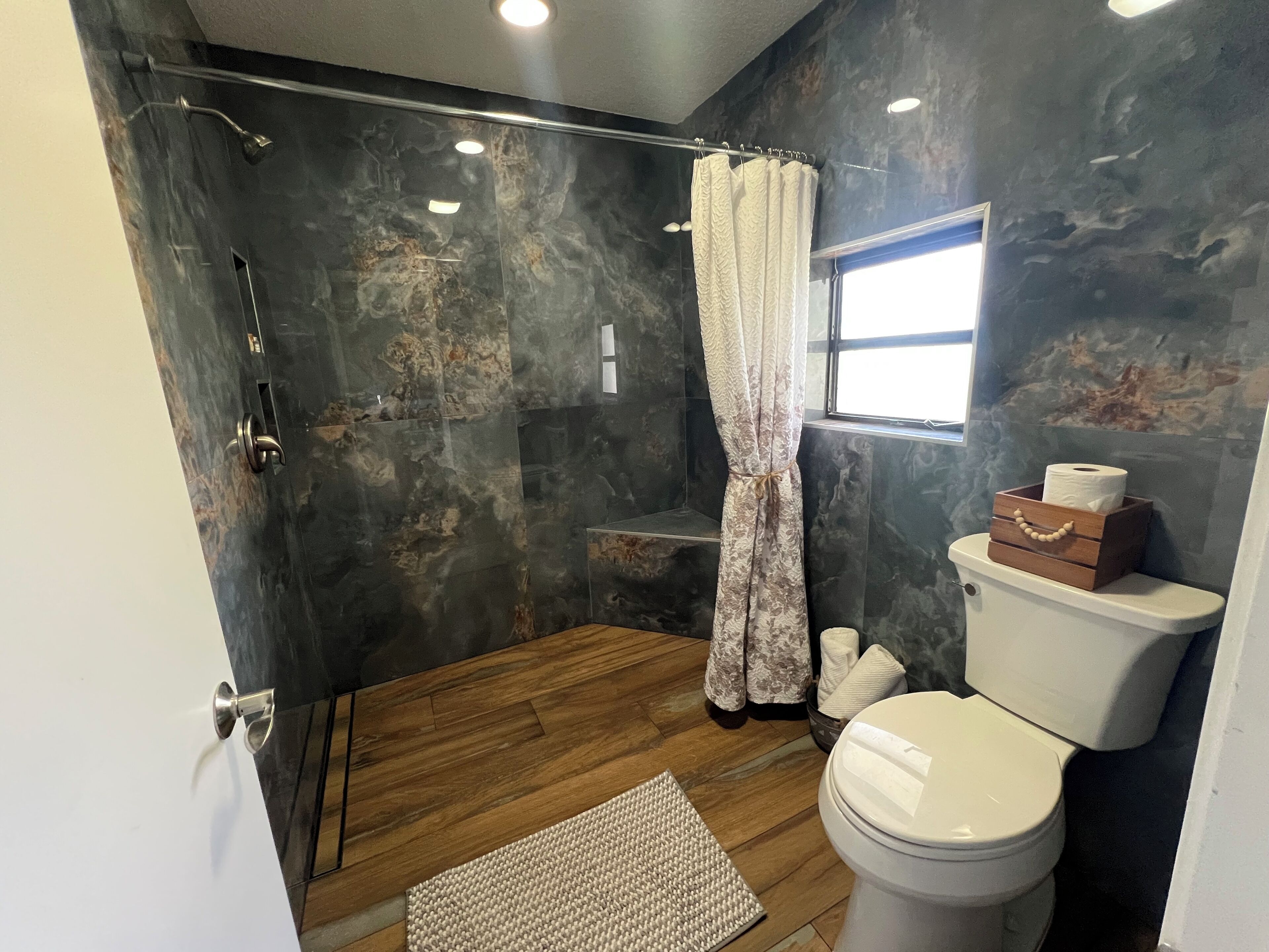 A bathroom with a shower, toilet, and a window.