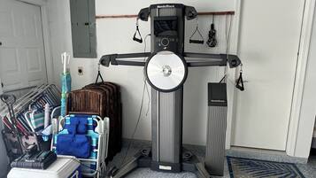 A room with a NordicTrack exercise machine, a blue cooler, and a cart with various items.