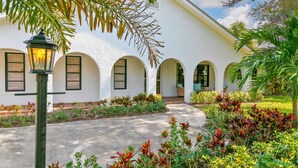 A building with a white exterior, multiple arched windows, and a well-maintained garden with various plants. - Peaceful and Spacious Pool home in Jensen Beach! RV-Boat Prkg-Fenced Yrd (Jensen Beach)