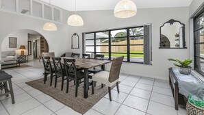 A spacious dining area with a large table and chairs, a woven pendant light, and a view of the outdoors through large windows. - Peaceful and Spacious Pool home in Jensen Beach! RV-Boat Prkg-Fenced Yrd (Jensen Beach)