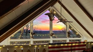 Ein Zimmer mit schrägem Dach, einem großen Fenster mit Sonnenuntergangsblick und einem Deckenventilator.