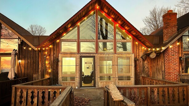 Eine rustikale Holzhütte mit großer Glasscheibe, einer Holzterrasse und Lichterketten.