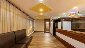 A reception area with a wooden reception desk, a sofa, and a wall with vertical blinds.