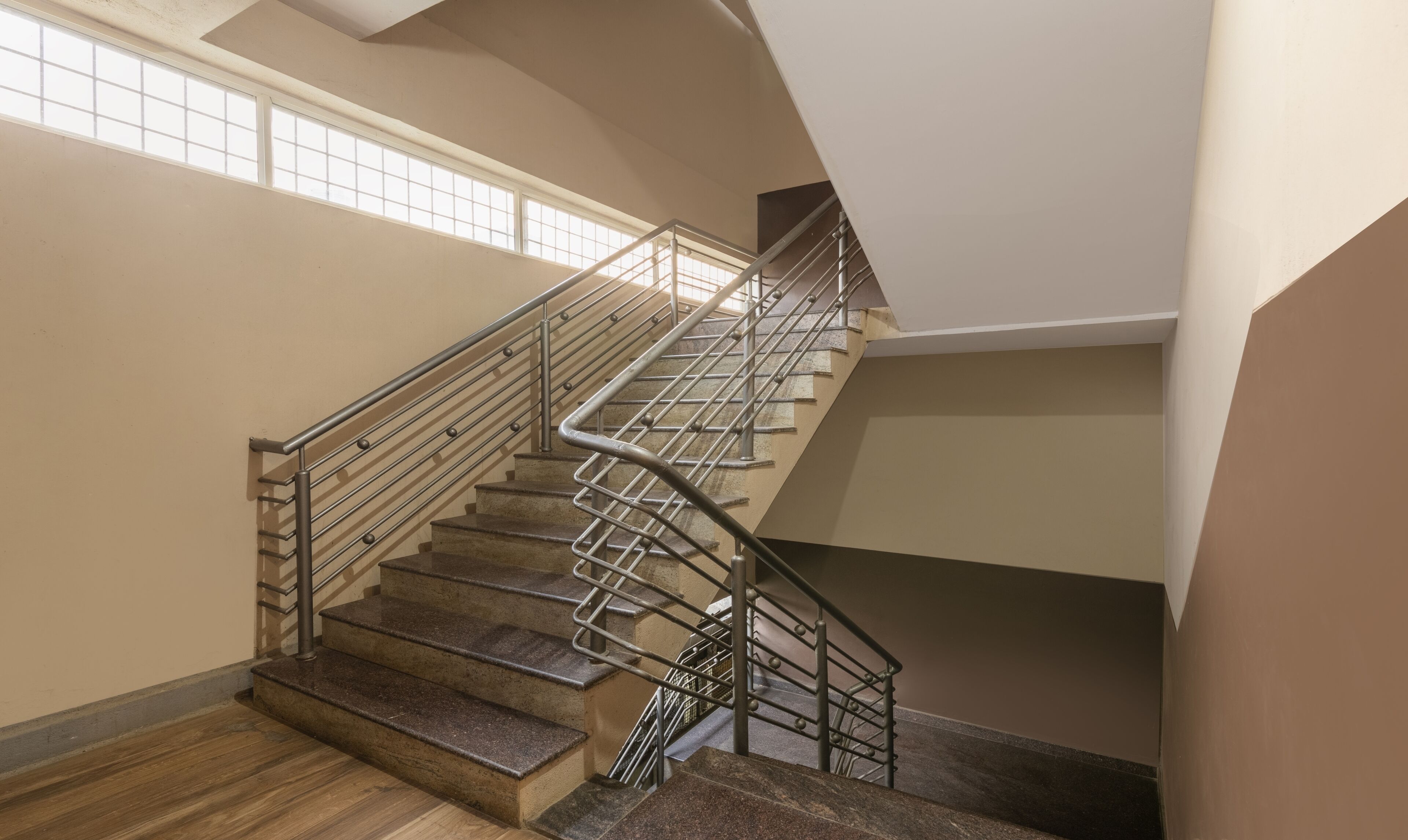Un interior de varios niveles con una escalera que tiene barandillas de metal y escalones de madera.