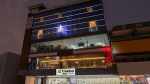 A multi-story building with a glass facade, a visible store named 'treebo' at the ground level, and a clear sky in the background.