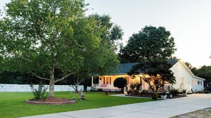 A single-story house with a front porch, a well-maintained lawn, and a white picket fence. - Cozy Country Retreat Ranch Style Home, private hot tub, pet friendly (Sanford)