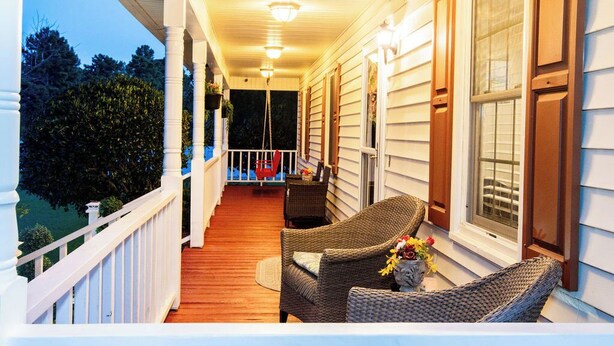A covered porch with wicker furniture and a small table, overlooking a backyard. - Cozy Country Retreat Ranch Style Home, private hot tub, pet friendly (Sanford)