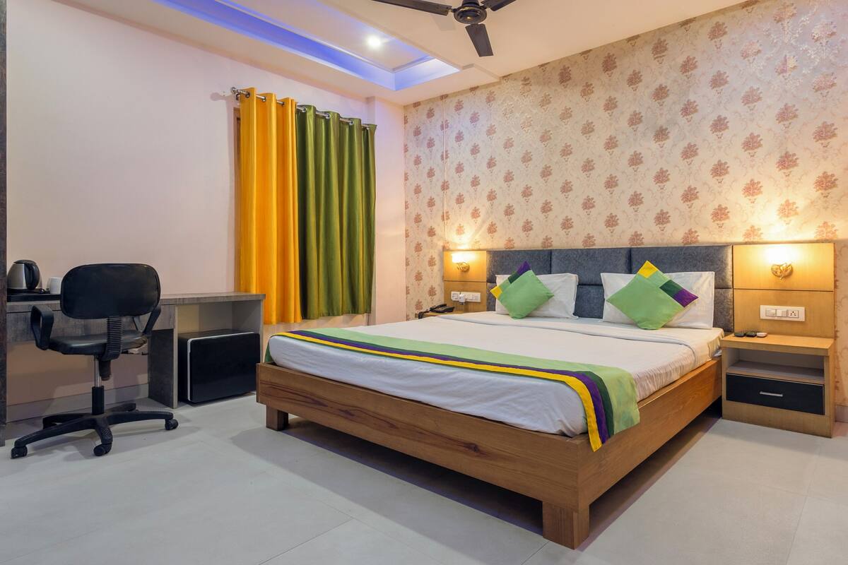 Een slaapkamer met een houten bed, een bureau met stoel, een plafondventilator en behang met een patroon.