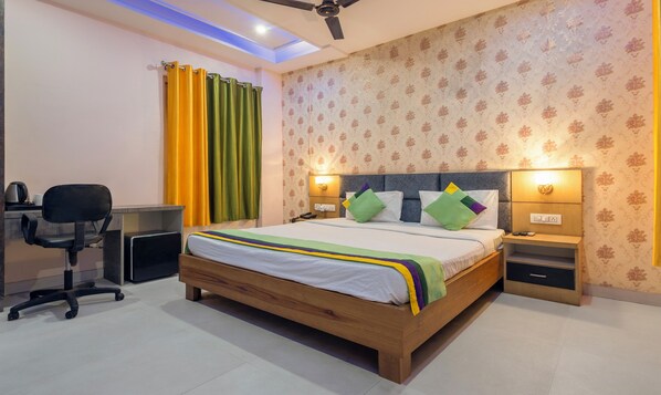 A bedroom with a wooden bed, a desk with a chair, a ceiling fan, and patterned wallpaper. - Treebo Shankuntalam, Near Lucknow Airport  (Lucknow)