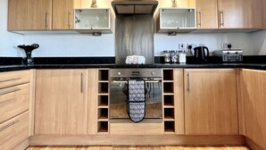 A kitchen with wooden cabinets, a stainless steel range hood, and a built-in oven with a hanging rack. - Modern Beachfront Bliss with Spectacular Views (Llanelli)