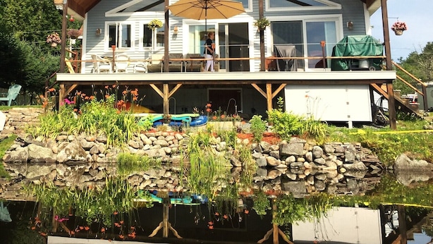 Ein zweistöckiges Haus mit Balkon, einer überdachten Terrasse und einem Teich im Vordergrund.