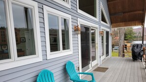 Eine überdachte Veranda mit zwei türkisfarbenen Adirondack-Stühlen, einer Glasschiebetür und Blick auf einen Garten mit Grill.