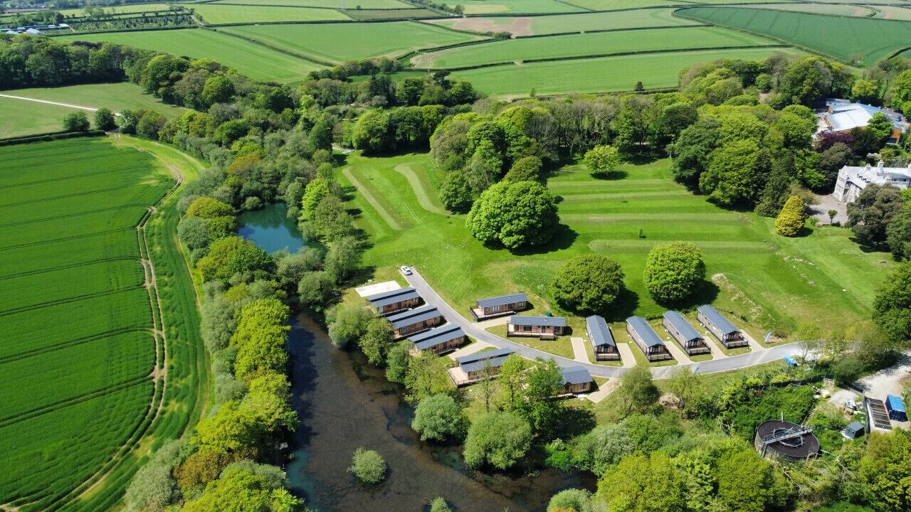 An aerial view of a rural property with a river, green fields, and a row of cabins.